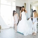 Female customers checking out dress worn by beautiful friend in bridal shop